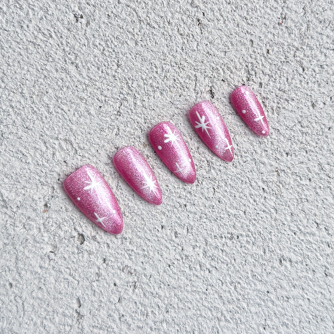 Almond-shaped press-on nails in party pink with shimmering cat-eye finish and twinkling four-point star designs. Perfect for parties and festive occasions.