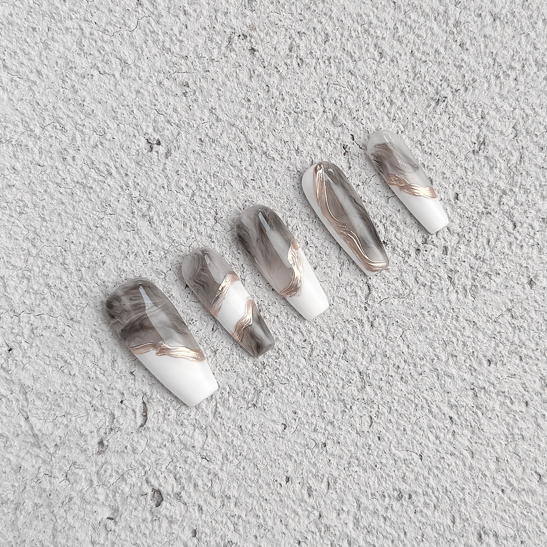 Handmade long coffin-shaped press-on nails with marble patterns and gold brushstroke accents, minimalist and elegant style