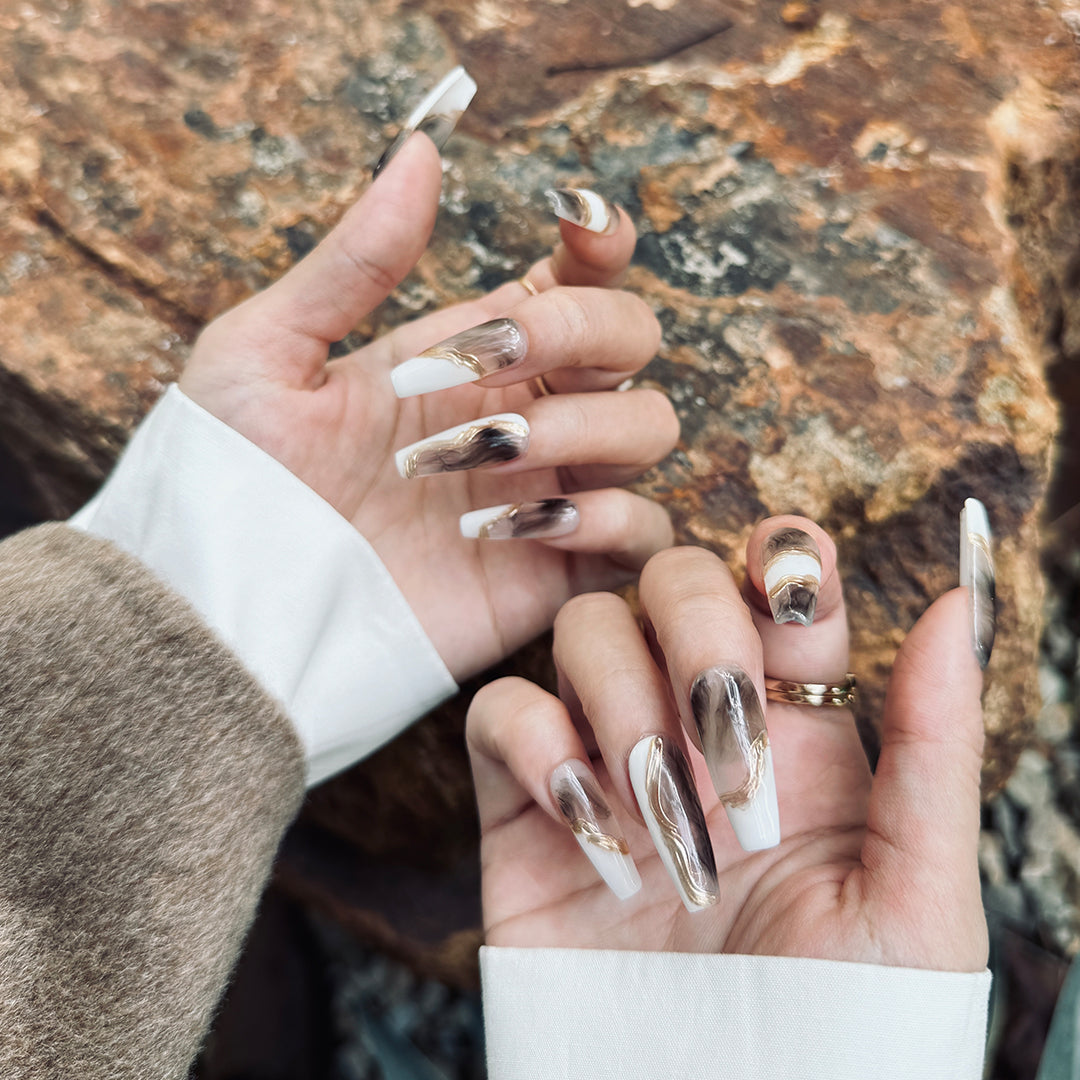 Handmade long coffin-shaped press-on nails with marble patterns and gold brushstroke accents, minimalist and elegant style