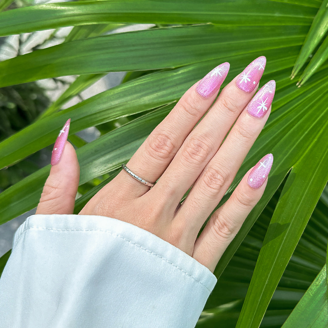Almond-shaped press-on nails in party pink with shimmering cat-eye finish and twinkling four-point star designs. Perfect for parties and festive occasions.
